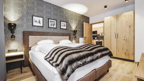 A stylish bedroom with a large bed and modern decor. The walls are gray with a geometric pattern, and a wooden wardrobe complements the furnishings. - Valentin Design Apartment - Sölden