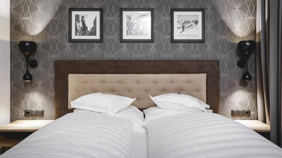 A modern bedroom with two separate beds and a stylish headboard. The walls are decorated with a geometric pattern, complemented by pretty pictures and elegant bedside lamps. - Valentin Design Apartment - Sölden