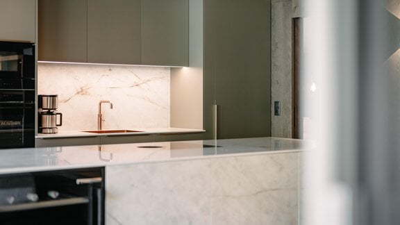 A modern kitchen with an elegant marble countertop and minimalist furniture. In the background, a stove and a coffee machine are visible. - VIBES Sölden - your alpine homebase - Sölden