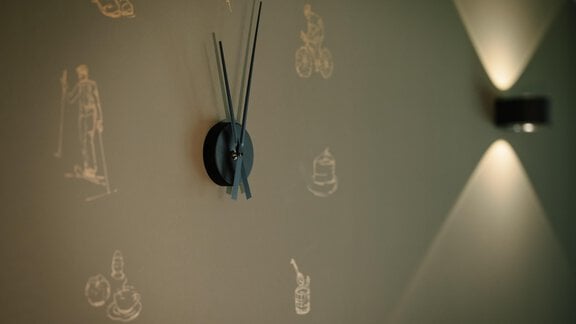 A stylish clock on a green wall with sketched motifs by the artist Anne-Sophie. Soft light on both sides of the clock creates a cozy atmosphere. - VIBES Sölden - your alpine homebase - Sölden