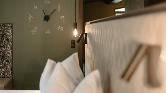 A stylish bedroom with a modern design and a green wall. On the wall, a clock and decorative elements are visible. - VIBES Sölden - your alpine homebase - Sölden