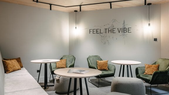 A modern lounge room with comfortable armchairs and round tables. The walls are painted in gentle shades and decorated with appealing lighting. - VIBES Sölden - your alpine homebase - Sölden