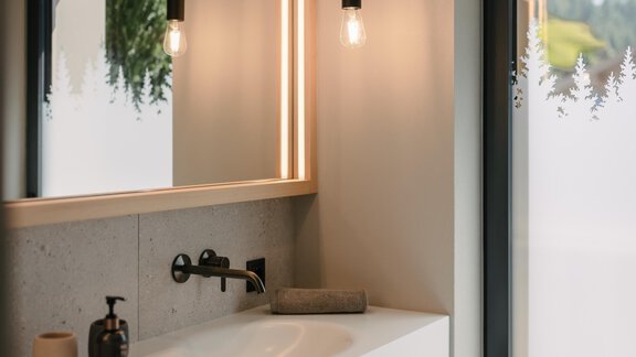 A modern bathroom with a large mirror and soft lighting. A view of nature through the window complements the cozy atmosphere. - VIBES Sölden - your alpine homebase - Sölden