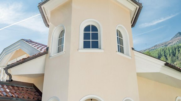 A modern, bright house with a distinctive turret-like design. The sky is clear and the surroundings are green and inviting. - Villa Castelbell - Sölden