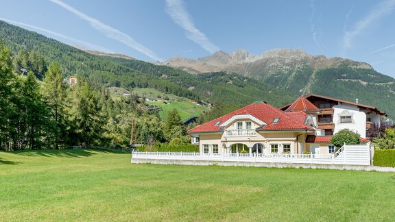 A beautiful house with a red roof in a green meadow. In the background, tall mountains and a clear sky can be seen. - Villa Castelbell - Sölden