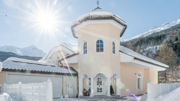 A beautiful house with a round turret and a bright facade in the snow. The sunny sky and the mountains in the background create a picturesque winter landscape. - Villa Castelbell - Sölden