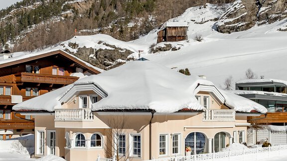 A beautiful house in the snow, surrounded by mountains and trees. The sky is clear with a few clouds. - Villa Castelbell - Sölden