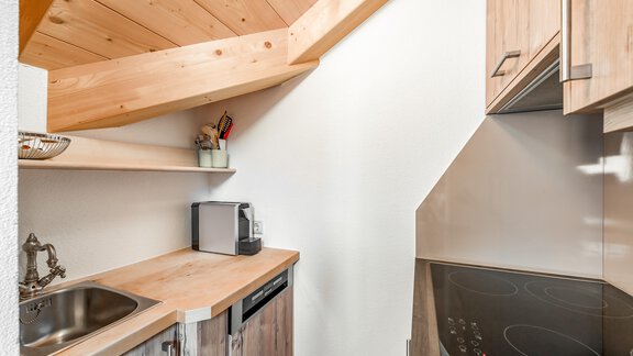 A small, modern kitchen with a wooden ceiling and bright furniture. It contains a sink, a cooktop, and a refrigerator. - Villa Castelbell - Sölden
