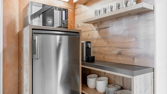 A modern kitchenette with a refrigerator and a microwave. On the shelves are dishes and cups in a cozy wooden setting. - Villa Castelbell - Sölden