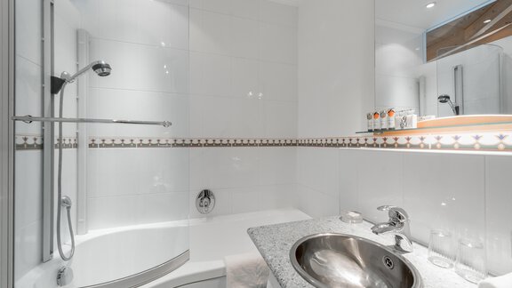 A modern bathroom with a shower and a bathtub. The sink area is equipped with an elegant stone surface. - Villa Castelbell - Sölden