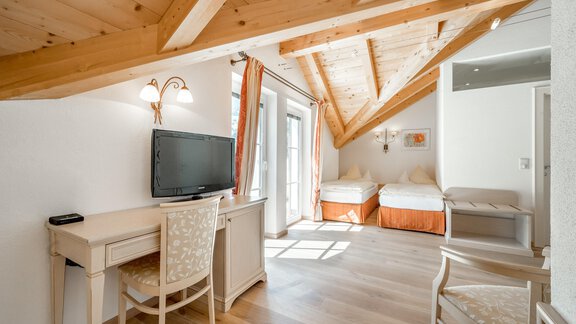 A bright room with a wooden beam ceiling and comfortable furniture. The room is equipped with a desk, a television, and a view outside. - Villa Castelbell - Sölden