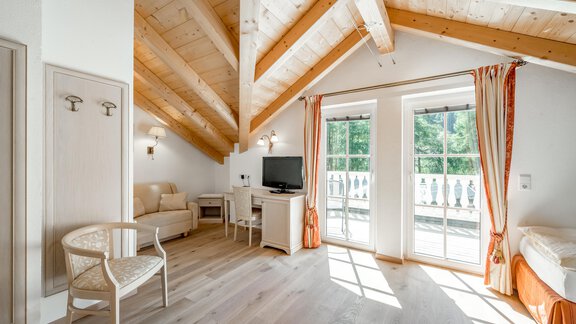 A bright room with a wooden ceiling and large windows. There is a television, a table and chairs, as well as a balcony. - Villa Castelbell - Sölden