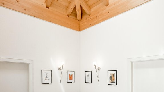 A bright room with a wooden ceiling and a table with chairs. Pictures hang on the walls, and there are two doors. - Villa Castelbell - Sölden