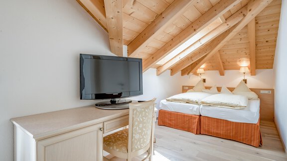 A cozy room in the attic with wooden ceilings and a large bed. A desk and a television are also located in the room. - Villa Castelbell - Sölden
