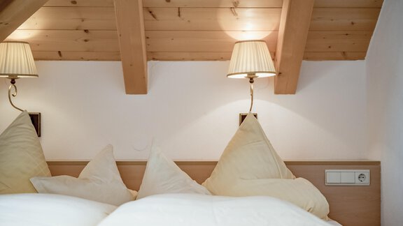 A cozy bedroom with soft pillows and warm light. The wooden ceiling creates an inviting atmosphere. - Villa Castelbell - Sölden