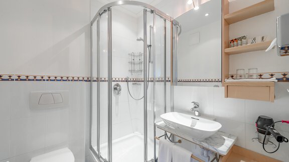 A modern bathroom with a shower cabin and a sink. The walls are light and there are practical shelves for toiletries. - Villa Castelbell - Sölden