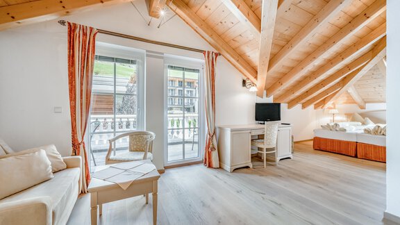 A cozy room with wooden paneling and large windows. There is a sofa, a table, and a television. - Villa Castelbell - Sölden