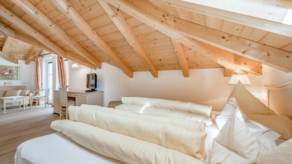 A cozy attic room with a wooden ceiling and plenty of daylight. Bed linens and pillows are neatly arranged on the bed. - Villa Castelbell - Sölden