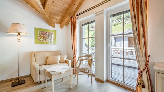 A cozy living room with a wooden ceiling and large windows. A sofa and a chair invite you to relax. - Villa Castelbell - Sölden