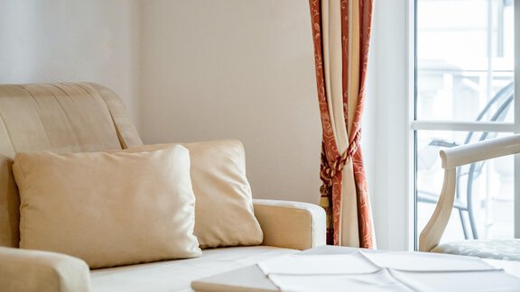 A bright living room with a beige sofa and a small table. Beautiful curtains hang in front of the windows. - Villa Castelbell - Sölden