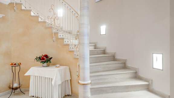 An elegant staircase with a curved railing leads upstairs. Next to the staircase is a table with a floral arrangement. - Villa Castelbell - Sölden