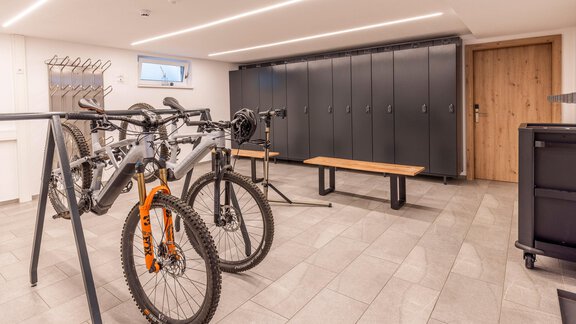 A modern bike room with several bicycles on a rack. In the background, there are black lockers and a wooden bench. - Vizensn Living - Sölden