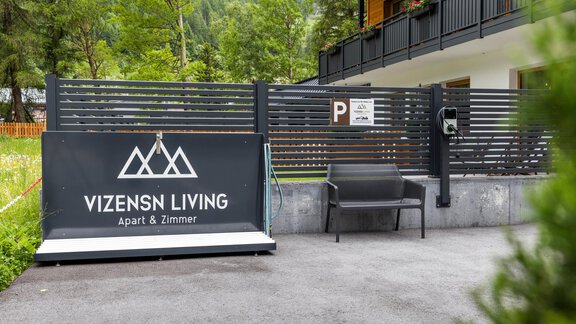 A modern entrance area with a sign saying "VIZENSN LIVING". In the background, trees and a building are visible. - Vizensn Living - Sölden