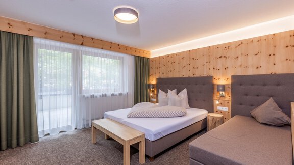 A bright and modern hotel room with two beds and a simple wooden design. Large windows provide plenty of natural light and a cozy atmosphere. - Vizensn Living - Sölden