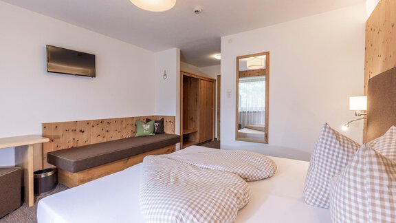 A modern hotel room with a double bed and two pillows. There is a large mirror and a cozy seating area with a television on the wall. - Vizensn Living - Sölden