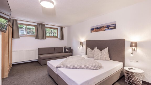 A modern bedroom with a large bed and bright walls. The room features a sofa and windows with curtains. - Vizensn Living - Sölden