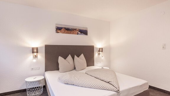 A modern bedroom with a large bed and stylish pillows. The walls are bright, and there is soft lighting for a cozy atmosphere. - Vizensn Living - Sölden