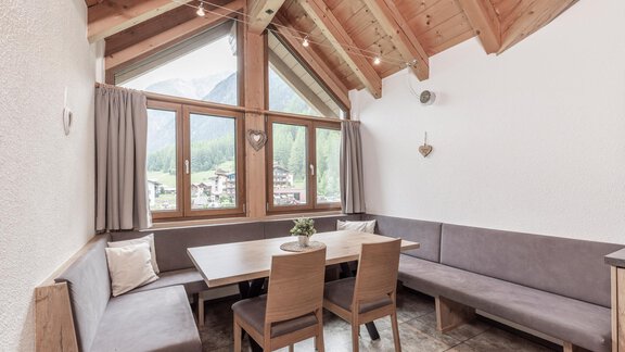 A cozy dining area with a wooden ceiling and large windows that offer a beautiful view. The furniture is simple and modern, perfect for relaxed gatherings. - Vizensn Living - Sölden