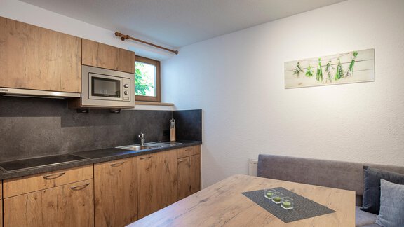 A modern kitchen with wooden cabinets and a cooking area. A dining area with a table and a cozy bench is also available. - Vizensn Living - Sölden