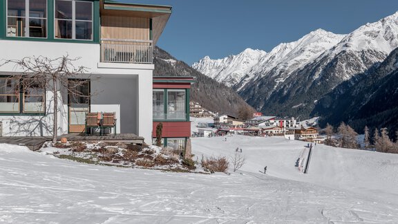 A modern building in a snowy landscape. In the background, majestic mountains and a small village are visible. - zuckerhütl NATURAPPART - Sölden