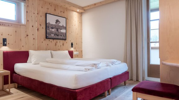 A modern bedroom with a large double bed and red upholstery. The walls are clad in light wood and there is a window with curtains. - zuckerhütl NATURAPPART - Sölden