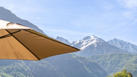 Eine schöne Berglandschaft mit schneebedeckten Gipfeln und grünem Tal. Im Vordergrund ist ein sonnenschirm zu sehen. - Apart Dorhoam - Umhausen