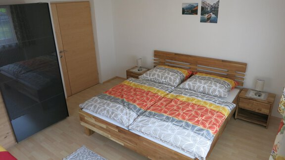 A bright bedroom with a large double bed and colorful duvet covers. Some photos hang on the wall and there is a wardrobe. - Apart Martina - Umhausen