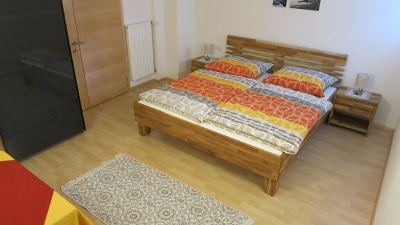 A cozy bedroom with a double bed and colorful bedding. The room is simply furnished and features a small table as well as a carpet. - Apart Martina - Umhausen