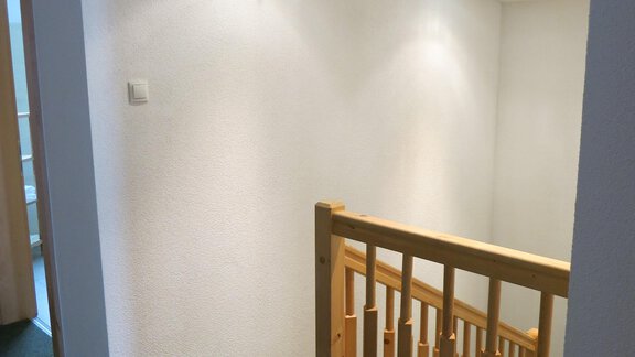 A bright stairwell with a wooden railing and plain walls. The lighting creates a pleasant atmosphere. - Apart Martina - Umhausen