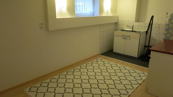 A bright room with a wooden floor and a cozy rug. In the corner, there is a small kitchenette with a sink. - Apart Martina - Umhausen