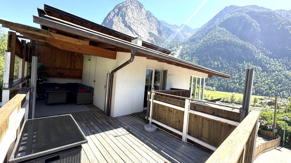Eine moderne Terrasse mit Holzbelag, umgeben von Bergen und grünen Wäldern. Der Raum ist hell und einladend, ideal für entspannte Stunden im Freien. - Appartement Bergglück - Umhausen
