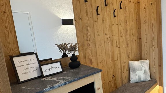 Ein moderner Eingangsbereich mit Holzverkleidung und einer Spiegelwand. Darunter befindet sich eine Bank und ein Möbelstück mit Schubladen. - Appartement Emilia - Umhausen