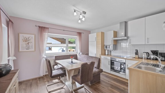 A modern kitchen with a dining table and chairs.  
Bright walls and windows create a friendly atmosphere. - Biancas Ferienwohnung im Haus Roswitha - Umhausen