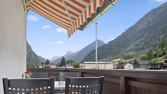 A cozy balcony overlooking mountains and a clear sky. The view shows a peaceful landscape with trees and small houses. - Biancas Ferienwohnung im Haus Roswitha - Umhausen