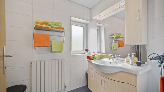 A modern bathroom with a sink and a large mirror. Colorful towels are neatly stored on a shelf. - Biancas Ferienwohnung im Haus Roswitha - Umhausen