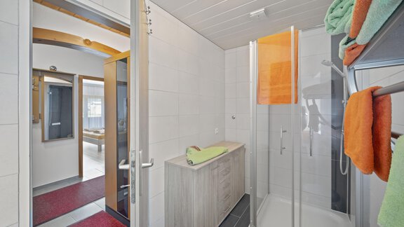 A modern bathroom with a shower and a wooden cabinet. Colorful towels hang on a towel rack. - Biancas Ferienwohnung im Haus Roswitha - Umhausen