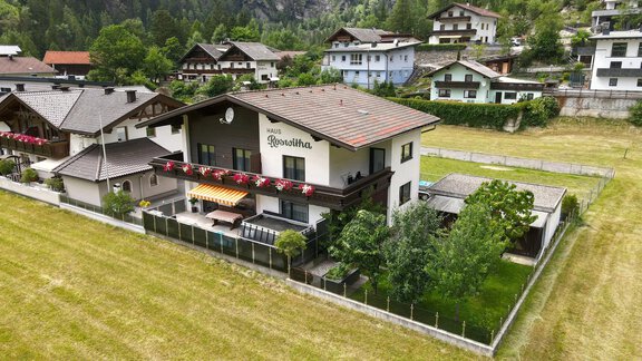 A large house with a garden and a terrace. It is located in a rural setting with other buildings in the background. - Biancas Ferienwohnung im Haus Roswitha - Umhausen