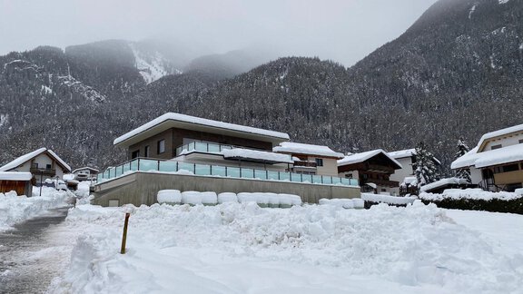 Ein modernes Haus in einer verschneiten Landschaft mit Bergen im Hintergrund. Der große Schnee bedeckt die Umgebung und verleiht der Szene eine ruhige Atmosphäre. - BLANKA'S Apart Auszeit - Umhausen