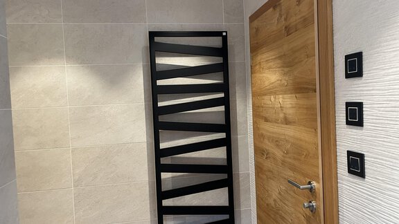 Ein modernes Badezimmer mit einem stilvollen Heizkörper und einer Holztür. Die Wände sind mit hellen Fliesen gestaltet. - BLANKA'S Apart Auszeit - Umhausen