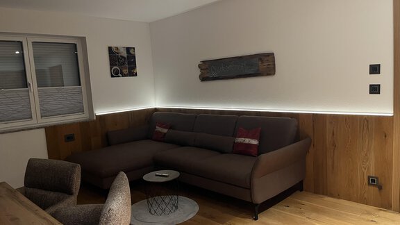 Ein modernes Wohnzimmer mit einem bequemen Sofa und einem Holztisch. Sanfte Beleuchtung und Holzvertäfelung sorgen für eine gemütliche Atmosphäre. - BLANKA'S Apart Auszeit - Umhausen
